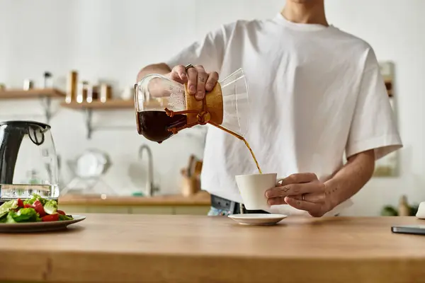 A man fills a white cup with aromatic coffee, enjoying a moment in a cozy kitchen. — Stock Photo