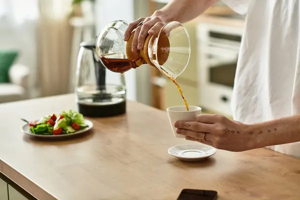 In einer sonnendurchfluteten Küche schenkt ein junger Mann Kaffee ein und genießt einen friedlichen Morgen. — Stockfoto