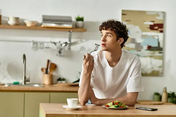 Em uma cozinha moderna e chique, um jovem de cabelos encaracolados saboreia uma refeição leve enquanto contempla a vida. — Stock Photo