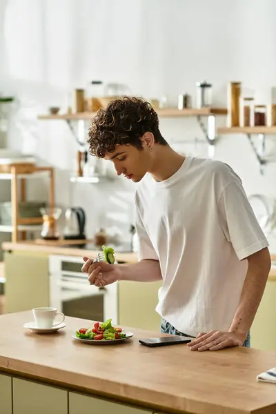 Un beau jeune homme dans une cuisine élégante assemble soigneusement une salade vibrante tout en profitant d'une matinée paisible. — Photo de stock
