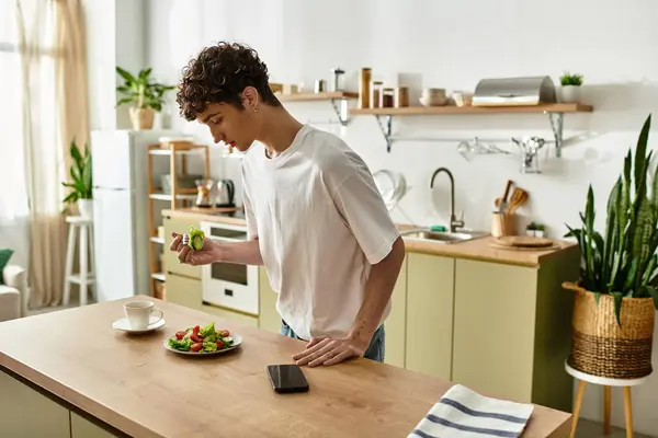 In a stylish kitchen, a handsome young man eating a colorful salad while enjoying his leisure time. — Stock Photo