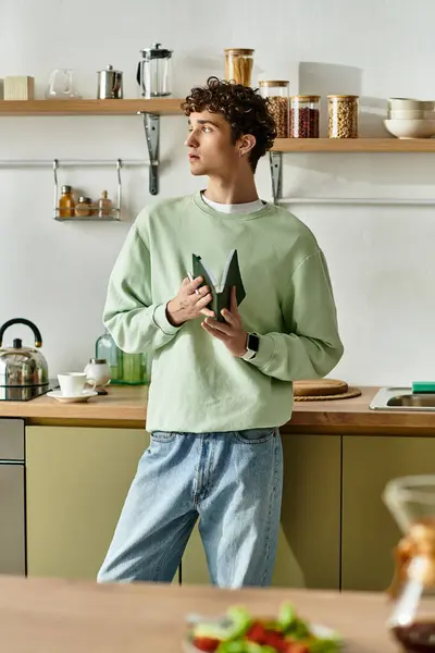 O jovem bonito em uma cozinha acolhedora contempla enquanto segura vegetais verdes frescos, exalando criatividade. — Stock Photo