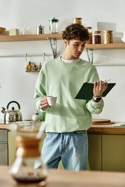 In einer hellen modernen Küche nippt ein gutaussehender junger Mann am Kaffee und konzentriert sich auf seine Notizen für ein Rezept.. — Stockfoto