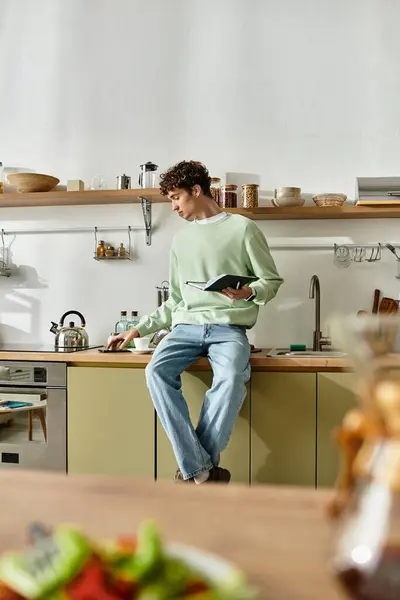 A handsome young man with curly hair reads a recipe while cooking in a stylish, modern kitchen atmosphere. — Stock Photo