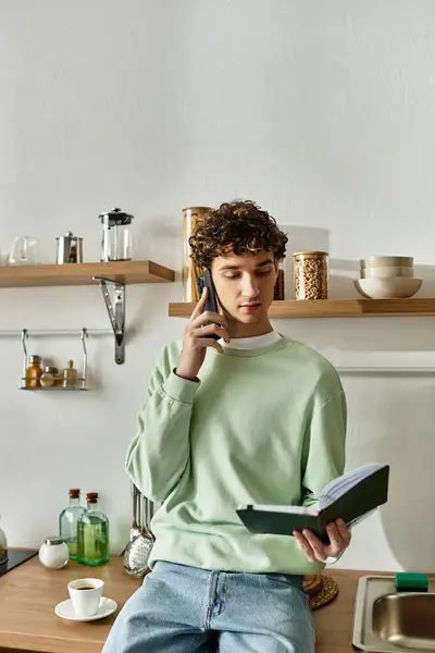 A handsome young man engages in a phone call while reviewing notes in a chic kitchen setting. — Stock Photo