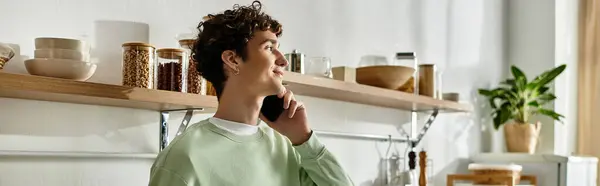 Um jovem elegante com chats cabelo encaracolado no telefone, rodeado por uma cozinha elegante e moderna e decoração fresca. — Fotografia de Stock