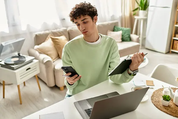 A young man with curly hair balances work-from-home tasks in a modern apartment, engaging with his tech. — Stock Photo