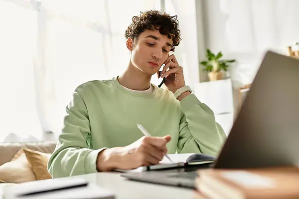 A handsome young man talks on the phone while jotting down notes at his stylish home workspace. — Stock Photo
