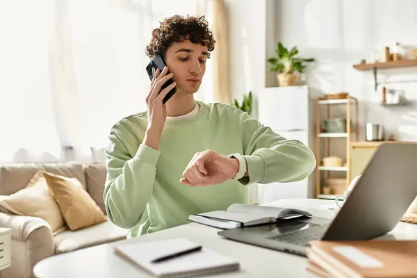 A handsome young man in a modern space manages tasks on his laptop while taking a phone call. — Stock Photo