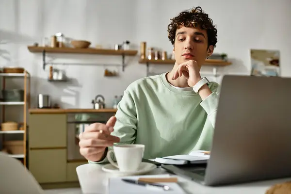A young man with curly hair sits in a modern apartment, deeply focused on his work while enjoying coffee. — Stock Photo