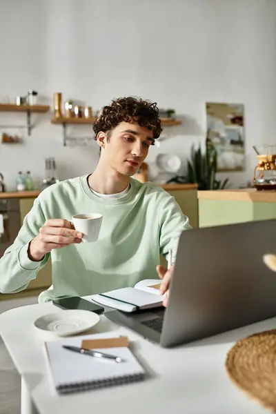 A young, handsome man enjoys coffee while diligently working from his stylish modern apartment setup. — Stock Photo
