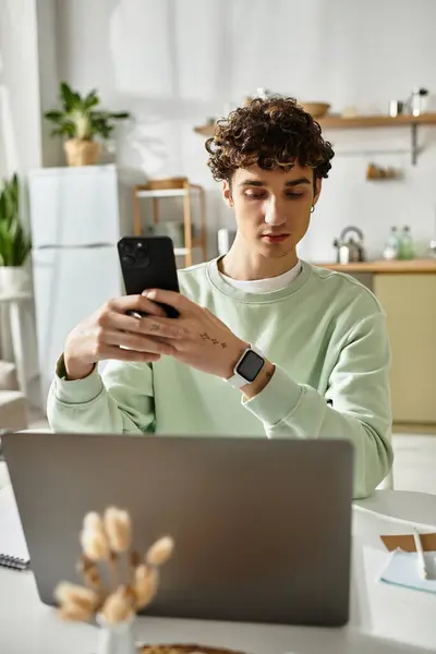 A handsome young man is engaged in remote work at his modern apartment, focused on his smartphone. — Stock Photo