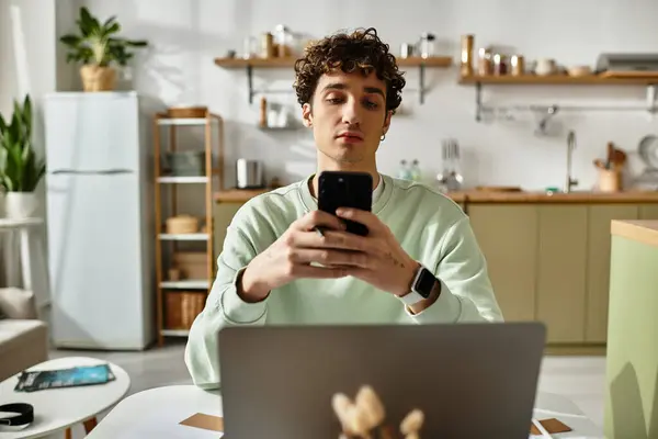 A young, handsome man with curly hair is concentrating on his smartphone while working at home. — Stock Photo