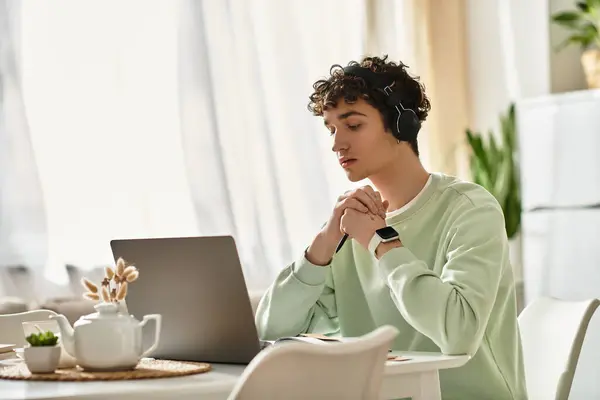 A young man with curly hair is focused on his work, surrounded by a bright and modern home environment. — Stock Photo
