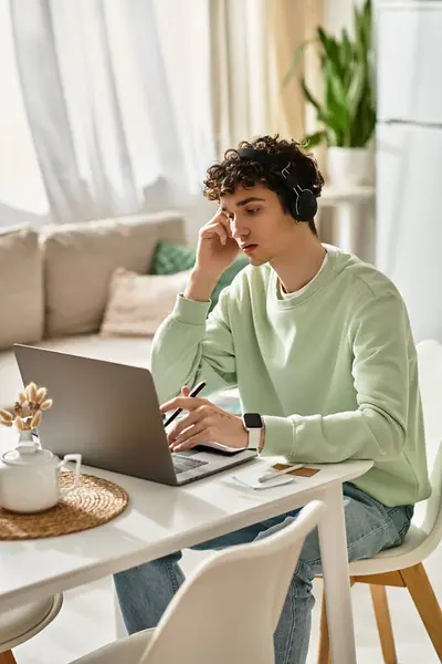 Un giovane uomo con i capelli ricci è profondamente impegnato in un lavoro remoto da un appartamento chic, circondato dalla luce naturale. — Foto stock