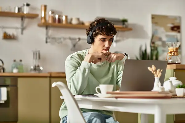 Un giovane lavora intensamente al suo computer portatile, immerso in compiti nel suo elegante spazio di lavoro domestico. — Foto stock