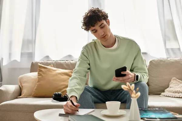 A handsome young man with curly hair writes notes while engaged in remote work at his chic apartment. — Stock Photo