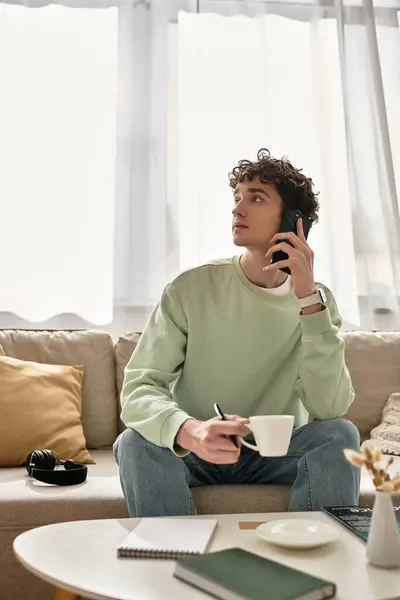 A curly-haired young man engages in work while savoring coffee in a bright, modern living space. — Stock Photo