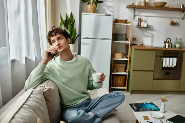 A handsome young man is engaged in a phone conversation while relaxing at home, sipping coffee. — Stock Photo