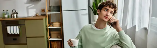 A handsome young man speaks on the phone while sipping coffee in a modern, bright living space. — Stock Photo