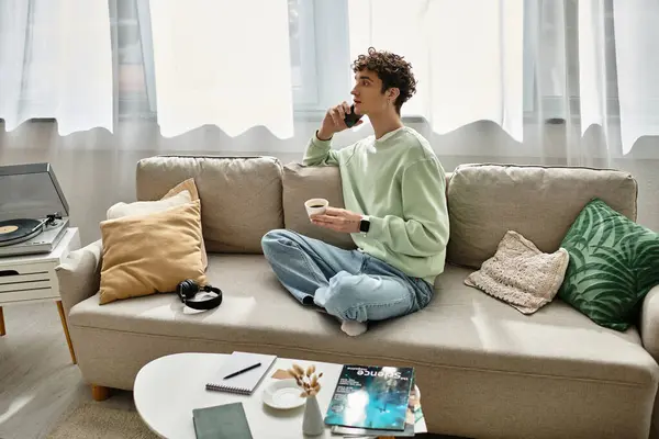 In a bright apartment, a handsome young man sips coffee and focuses on his laptop while relaxing on the couch. — Stock Photo