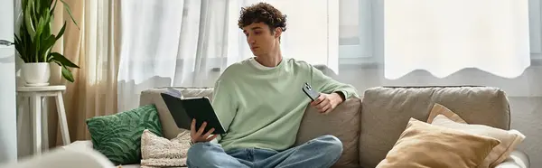 A handsome young man relaxes in his contemporary living space, immersed in an engaging book. — Stock Photo