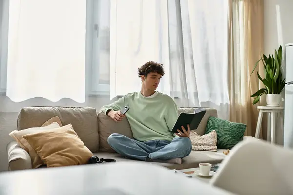 Ein fokussierter junger Mann sitzt gemütlich in einer stilvollen Wohnung, liest und arbeitet in gemütlicher Atmosphäre. — Stockfoto