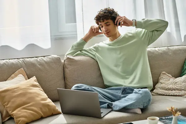 A stylish young man sits comfortably on his couch, engaged in his work from home while wearing headphones. — Stock Photo