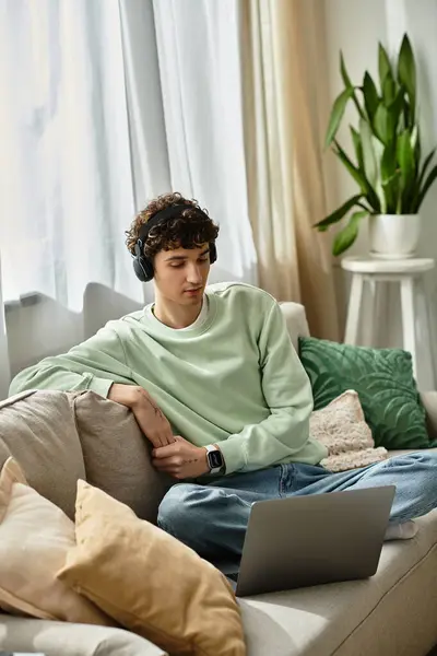 A young man with curly hair is focused on his laptop while working from the comfort of his stylish living space. — Stock Photo