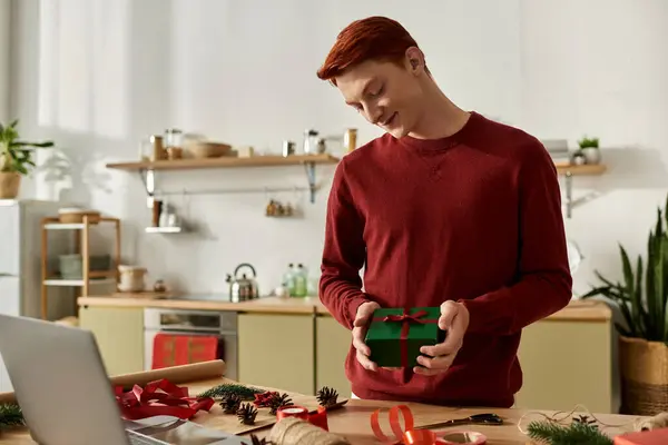 A young man stands in a warmly decorated kitchen, admiring a beautifully wrapped Christmas gift. — Stock Photo