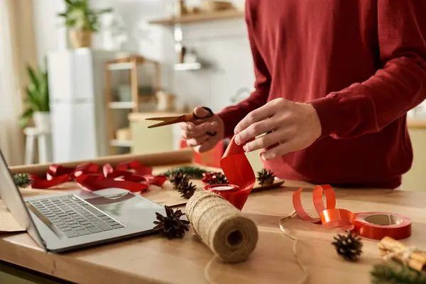 A young man wraps Christmas gifts in a warm kitchen with red ribbons and natural accents. — Stock Photo