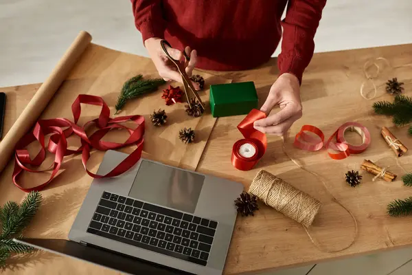 The young man is wrapping Christmas gifts with colorful ribbons and pinecones around him. — Stock Photo