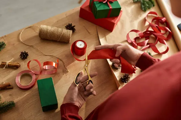 Un jeune homme se concentre sur la création de beaux emballages cadeaux avec des rubans vibrants et des accessoires de vacances. — Photo de stock