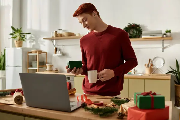 With a warm smile, a young man holds a gift while sipping a drink in a festive kitchen. — Stock Photo