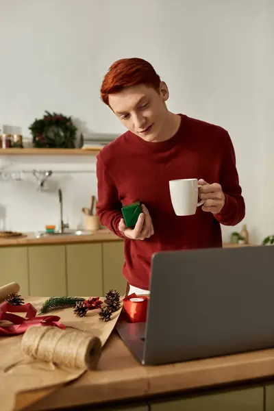 In a cozy kitchen, a young man sips a warm drink and wraps Christmas gifts with joy. — Stock Photo