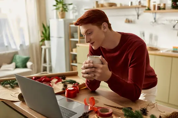 Un joven está maravillosamente inmerso en la planificación de vacaciones, sosteniendo una bebida caliente en sus manos. - foto de stock