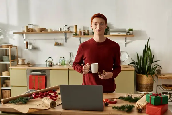 In einer festlichen Küche genießt ein junger Mann ein warmes Getränk, umgeben von weihnachtlicher Dekoration. — Stockfoto