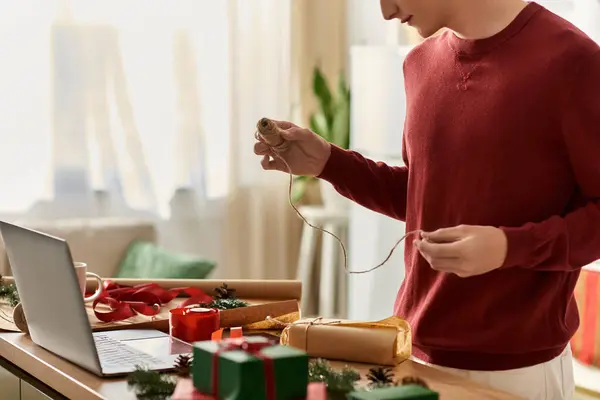 A young man wraps Christmas gifts thoughtfully while enjoying the holiday spirit indoors. — Stock Photo