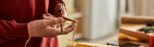 A young man carefully cuts twine for wrapping Christmas gifts in a warm, festive environment. — Stock Photo