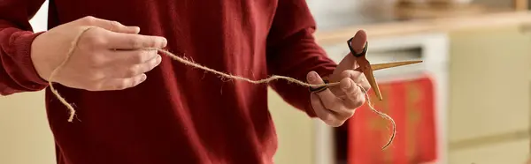 The young man clips a length of twine in a warm kitchen filled with holiday spirit. — Stock Photo