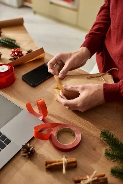 A young man skillfully wraps Christmas presents, surrounded by decorative items and supplies. — Stock Photo