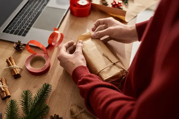 Sorgfältig wickelt der junge Mann ein Geschenk ein, umgeben von Weihnachtsdekoration und Vorräten.. — Stockfoto