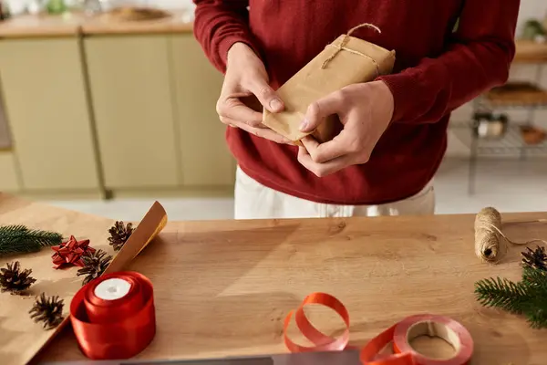 A young man in a red sweater wraps a Christmas gift amid festive decor. — Stock Photo