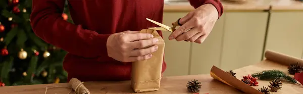 A young man wraps a present with care at home, surrounded by holiday decorations and cheer. — Stock Photo