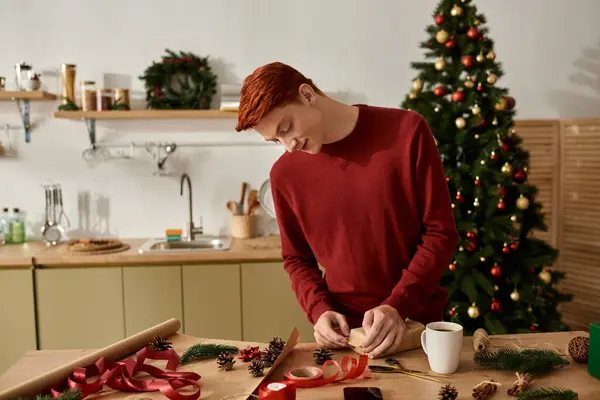 A young man is wrapping gifts at a beautifully decorated kitchen for Christmas festivities. — Stock Photo