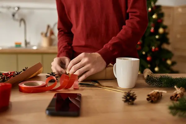 The young man carefully wraps gifts on a wooden table adorned with festive decorations. — Stock Photo