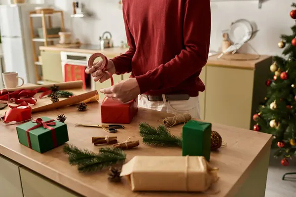 A young man wraps gifts in a festive kitchen filled with Christmas decor and supplies. — Stock Photo