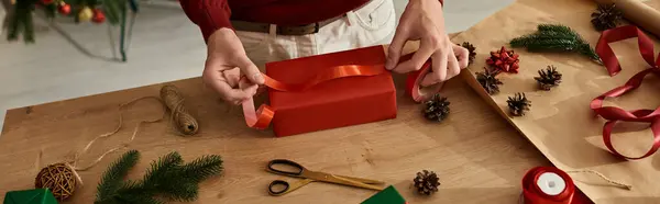 Un joven envuelve un regalo de Navidad con una cinta brillante, listo para las vacaciones. - foto de stock