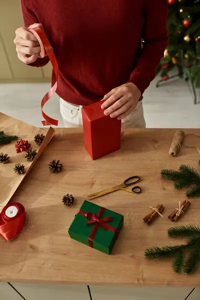 The young man meticulously decorates Christmas gifts using ribbon and festive elements at home. — Stock Photo