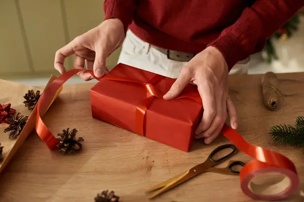 A young man meticulously wraps a festive gift using vibrant red ribbon, exuding holiday cheer. — Stock Photo